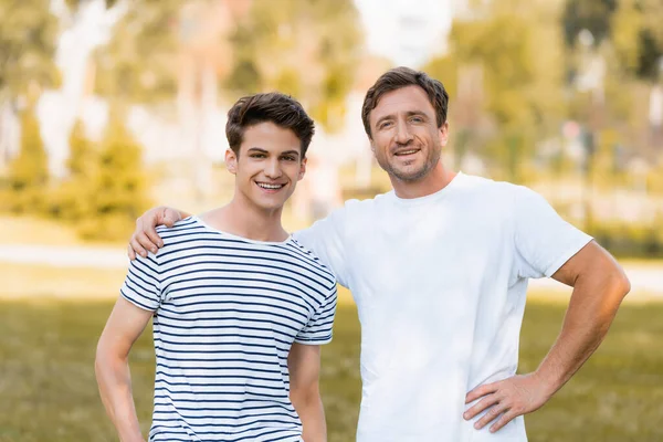 Man standing with hand on hip and hugging teenager son outside — Stock Photo