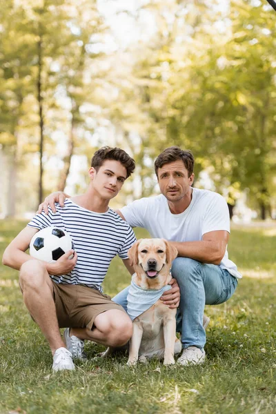 Батько сидить біля підліткового сина з футболом і золотим ретривером — стокове фото