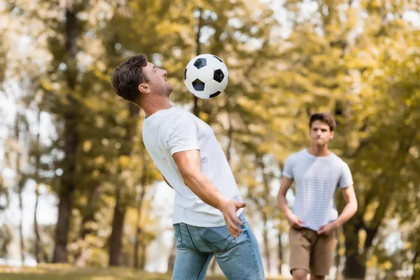 Focus selettivo del padre che gioca a calcio vicino al figlio adolescente nel parco — Foto stock