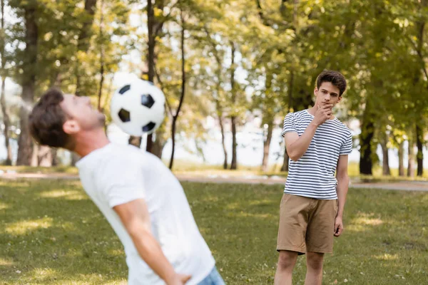 Enfoque selectivo de hijo adolescente pensativo mirando a padre jugando fútbol - foto de stock