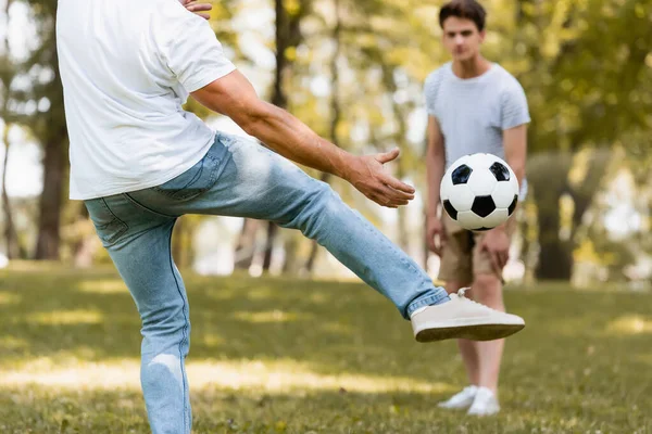 Selective focus of father kicking football near teenager son — Stock Photo