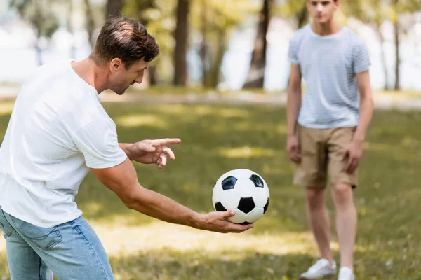 Enfoque selectivo de padre sosteniendo el fútbol en la mano cerca de hijo adolescente - foto de stock