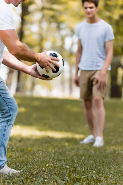 Foco seletivo do homem segurando o futebol na mão perto do filho adolescente — Fotografia de Stock