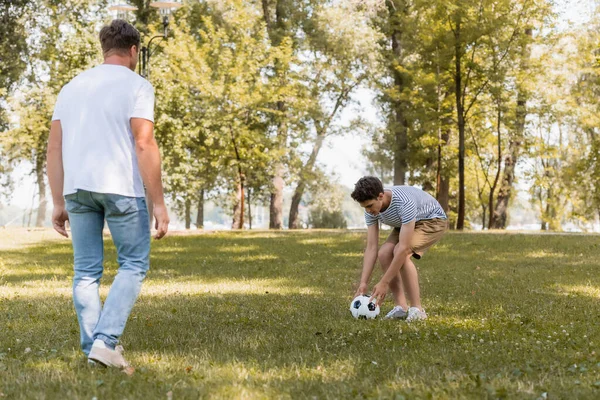 Enfoque selectivo de hijo adolescente tocando fútbol cerca del padre - foto de stock