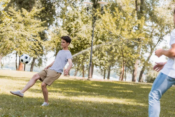 Enfoque selectivo de hijo adolescente jugando al fútbol con el padre en el parque - foto de stock