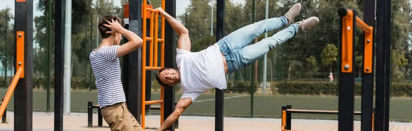 Panoramic crop of teenager son touching head while looking at sportive father exercising on horizontal bars — Stock Photo