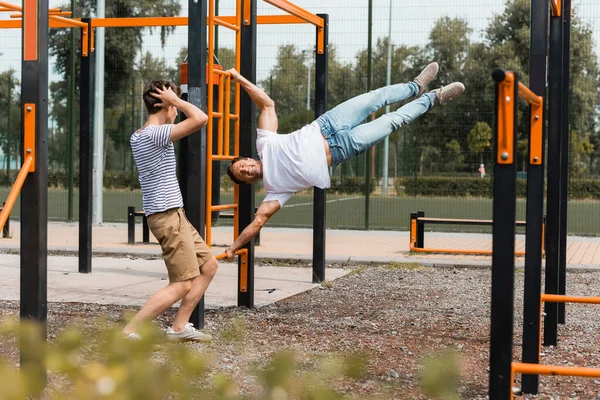 Enfoque selectivo del hijo adolescente tocando la cabeza mientras mira al padre deportivo haciendo ejercicio en barras horizontales - foto de stock