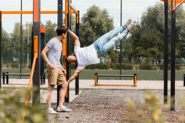 Selective focus of teenager son looking at sportive father exercising on horizontal bars — Stock Photo