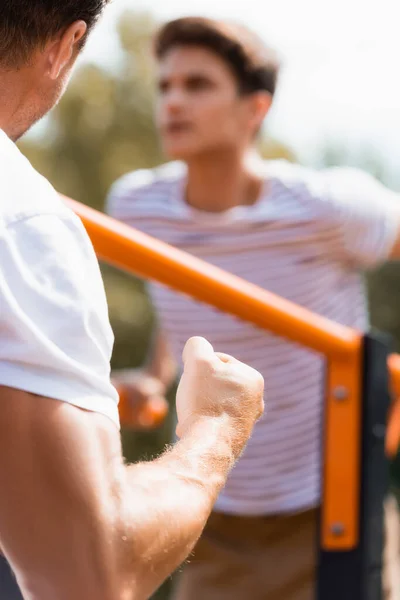 Selective focus of father with clenched fist near teenager son exercising on horizontal bars — Stock Photo