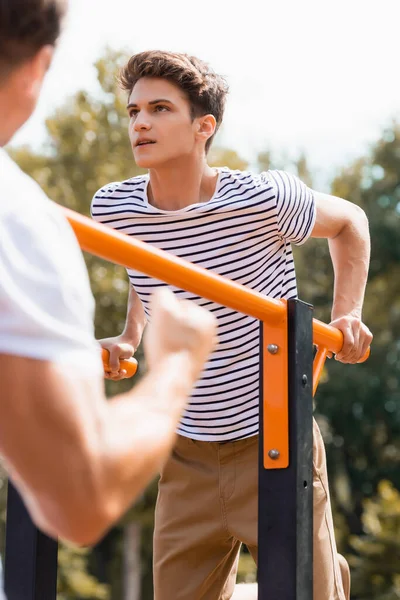 Selective focus of teenager boy exercising on horizontal bars near father — Stock Photo