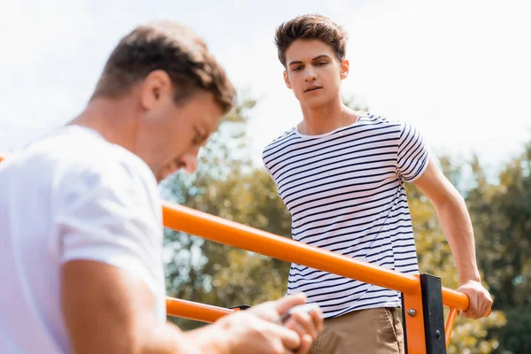 Selective focus of teenager boy exercising on horizontal bars and looking at father — Stock Photo