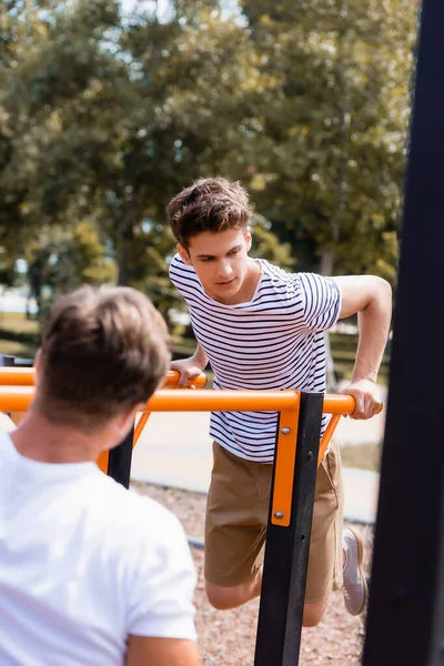 Foco seletivo do adolescente menino exercendo em barras horizontais perto do homem — Fotografia de Stock