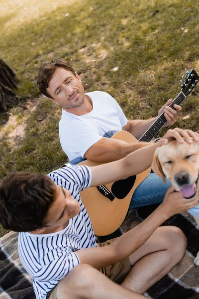 Mann hält Akustikgitarre in der Hand und kuschelt Golden Retriever mit Teenager-Sohn — Stockfoto