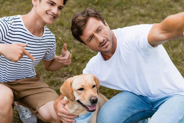 Teenager boy pointing with fingers at golden retriever near father — Stock Photo