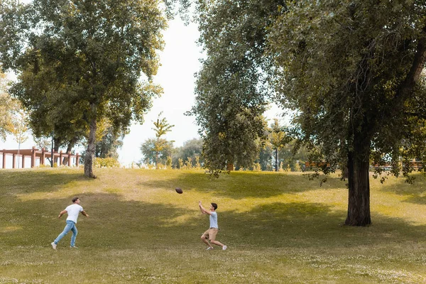 Padre e hijo adolescente jugando fútbol americano en el parque verde - foto de stock