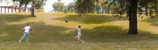 Cabeçalho do site de pai e filho adolescente jogando futebol americano no parque verde — Fotografia de Stock