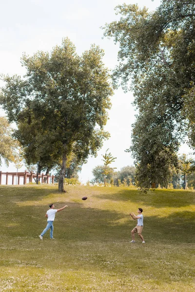 Padre y adolescente niño jugando fútbol americano en el parque verde - foto de stock