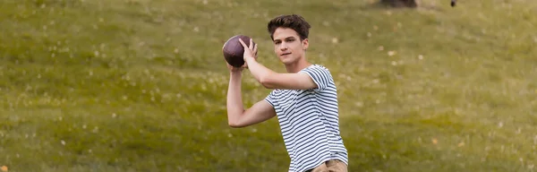 Панорамный урожай подростка, играющего в американский футбол в парке — стоковое фото