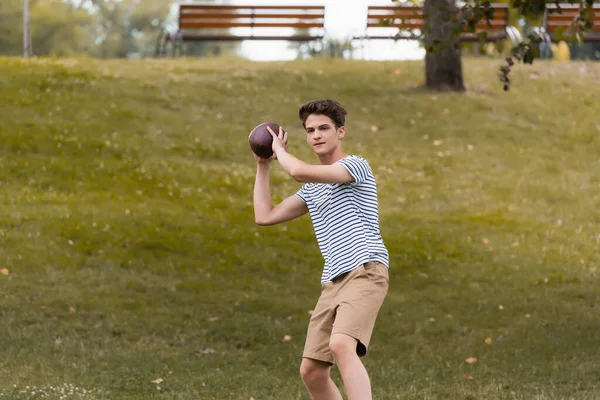 Adolescent garçon jouer au football américain dans green park — Photo de stock