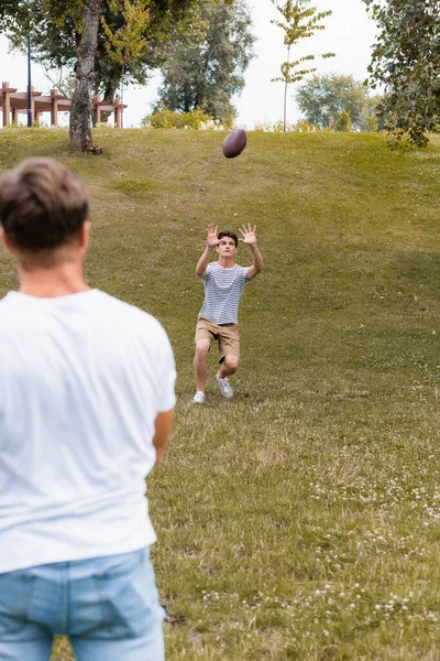 Messa a fuoco selettiva del figlio adolescente cattura palla da rugby vicino al padre nel parco — Foto stock