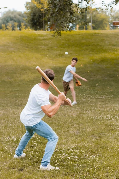 На заднем плане отец держит бейсбольную биту во время игры в бейсбол с мальчиком-подростком — стоковое фото