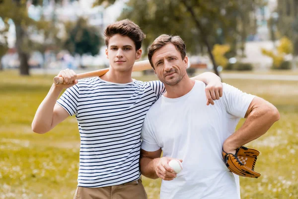 Adolescente menino com morcego softball de pé perto do pai em luva de couro segurando bola — Fotografia de Stock