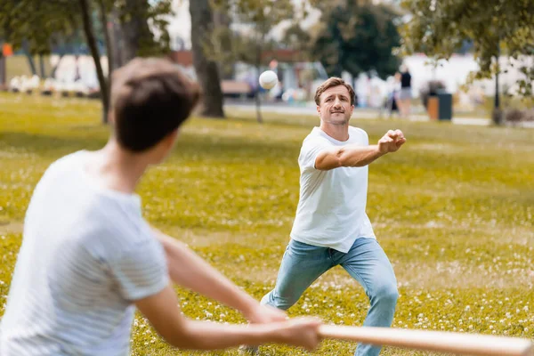 Enfoque selectivo de padre lanzando pelota jugando béisbol con hijo en el parque - foto de stock