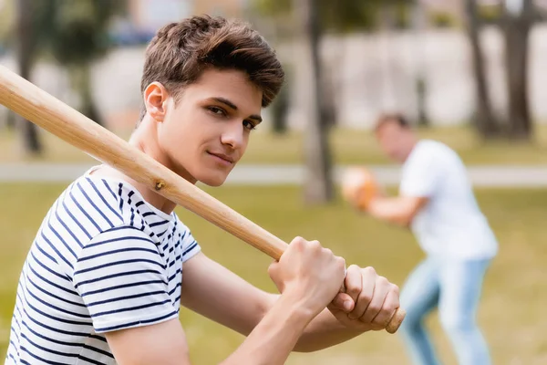 Foco seletivo do filho adolescente com morcego softball olhando para a câmera enquanto joga beisebol com o pai no parque — Fotografia de Stock