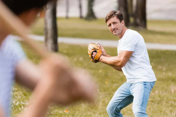 Selective focus of concentrated father in leather glove playing baseball with teenager son in park — Stock Photo