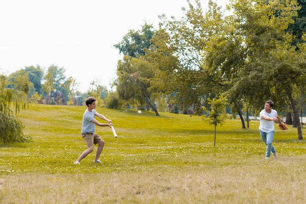 Мальчик-подросток держит бейсбольную биту и играет в бейсбол с отцом в зеленом парке — стоковое фото