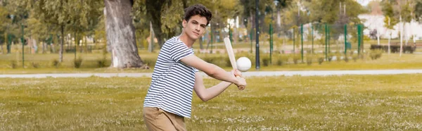 Панорамный снимок мальчика-подростка, держащего в руках бейсбольную биту и играющего в парке — стоковое фото