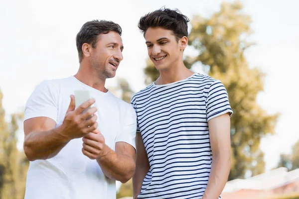 Adolescente gioioso che guarda smartphone in mani di padre — Foto stock