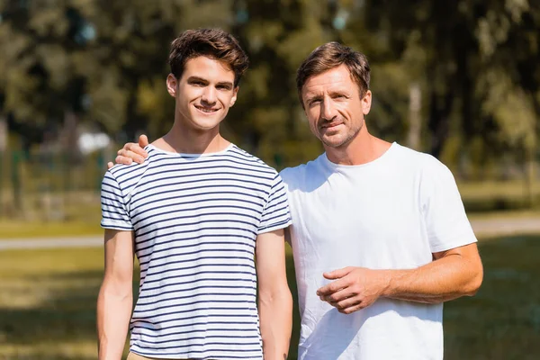 Père debout et étreignant fils adolescent dans le parc — Photo de stock