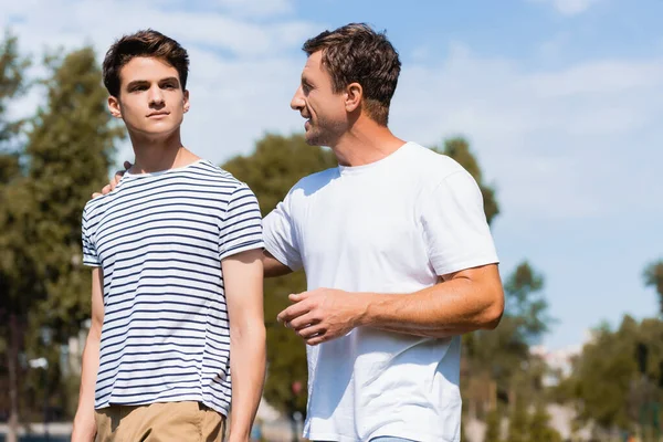 Father hugging and looking at teenager son in park — Stock Photo
