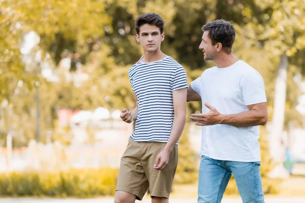 Père marche, gestuelle et parler avec le fils adolescent dans le parc — Photo de stock