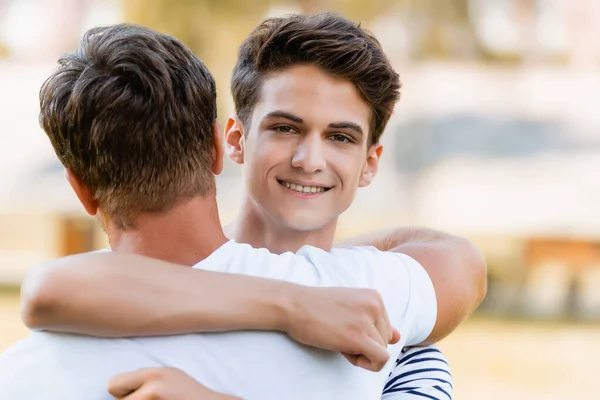 Vista posteriore del padre che abbraccia gioioso figlio adolescente fuori — Foto stock