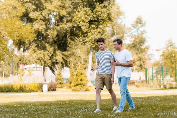 Homme geste tout en marchant et parler avec adolescent fils dans le parc — Photo de stock