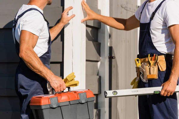 Cropped view of builders with toolbox and tool belt standing near facade of building outdoors — Stock Photo