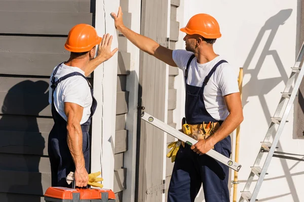 Builders in uniform and hardhats touching facade of building outdoors — Stock Photo