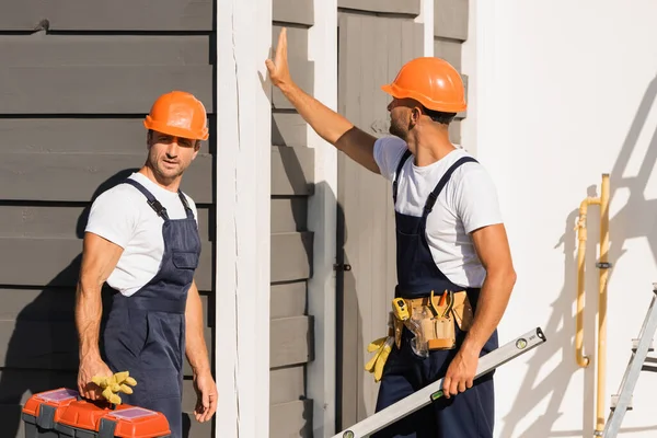 Constructeurs en salopette tenant la boîte à outils et le niveau d'esprit près du bâtiment à l'extérieur — Photo de stock