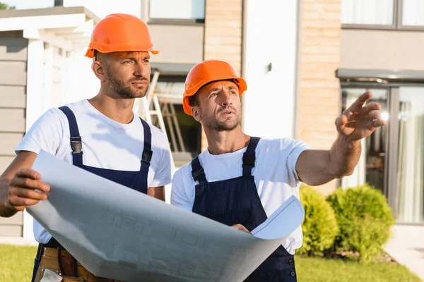 Builder pointing with hand near colleague with blueprint outdoors — Stock Photo