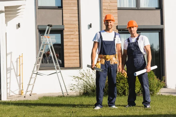 Constructores en ropa de trabajo manteniendo el nivel de espíritu y el plano en el césped cerca de la construcción - foto de stock