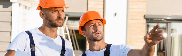 Panoramic shot of builder pointing with hand near colleague outdoors — Stock Photo
