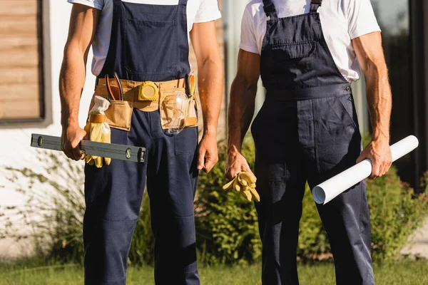 Cropped view of builders with blueprint and tool belt outdoors — Stock Photo