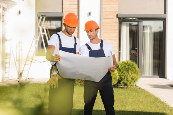 Foco seletivo de construtores em macacões e hardhats olhando para o modelo perto do edifício — Fotografia de Stock