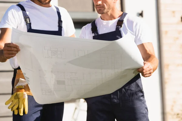 Cropped view of builders looking at blueprint outdoors — Stock Photo
