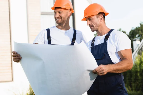 Construtores em chapéus duros e uniforme segurando planta ao ar livre — Fotografia de Stock