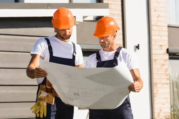 Builders holding blueprint while working near building — Stock Photo