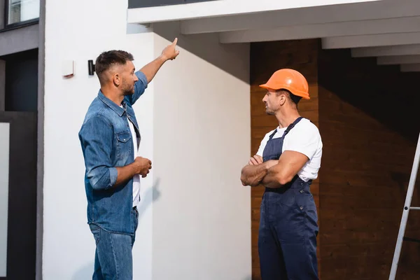 Client pointant du doigt la façade du bâtiment près de l'ouvrier à l'extérieur — Photo de stock