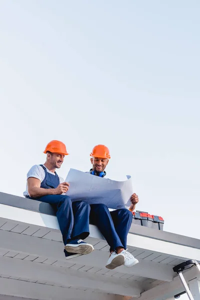 Visão de baixo ângulo dos trabalhadores segurando o modelo enquanto se sentam perto da caixa de ferramentas no telhado do edifício — Fotografia de Stock